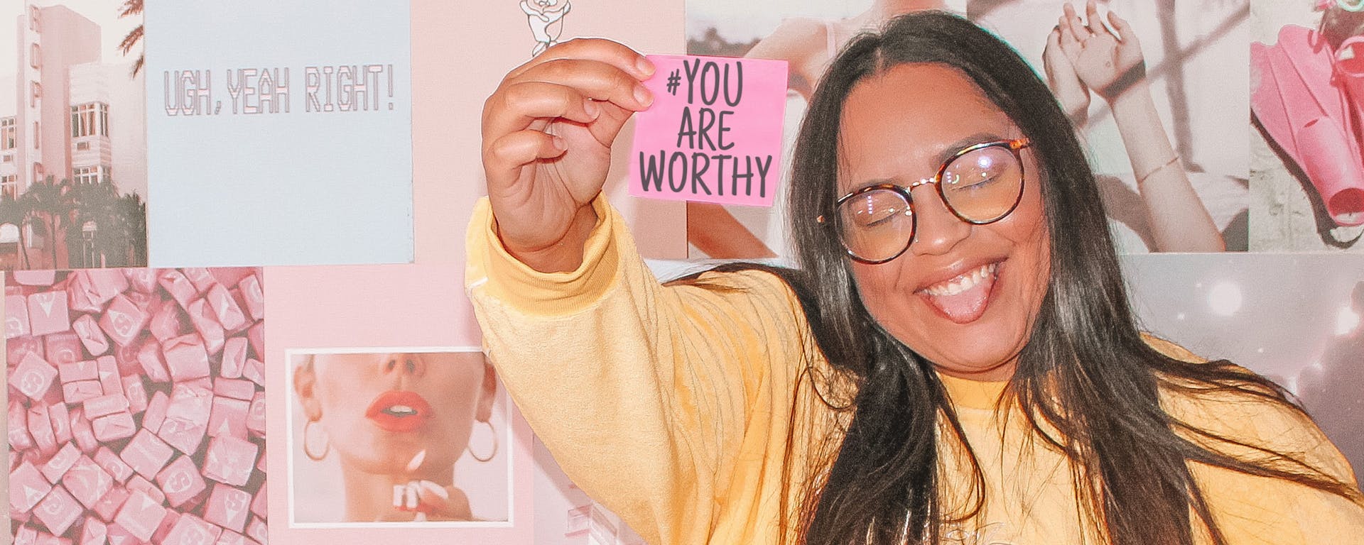 A women, smiling and holding a sign that says "You Are Worthy"