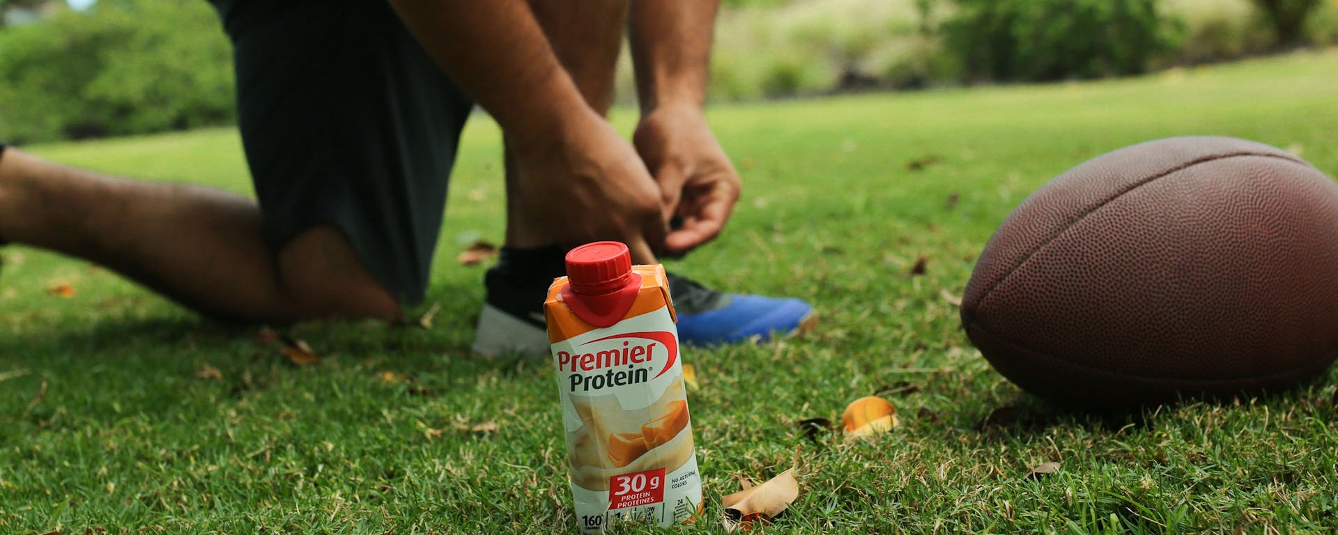 An athlete with a Premier Protein drink and a football.